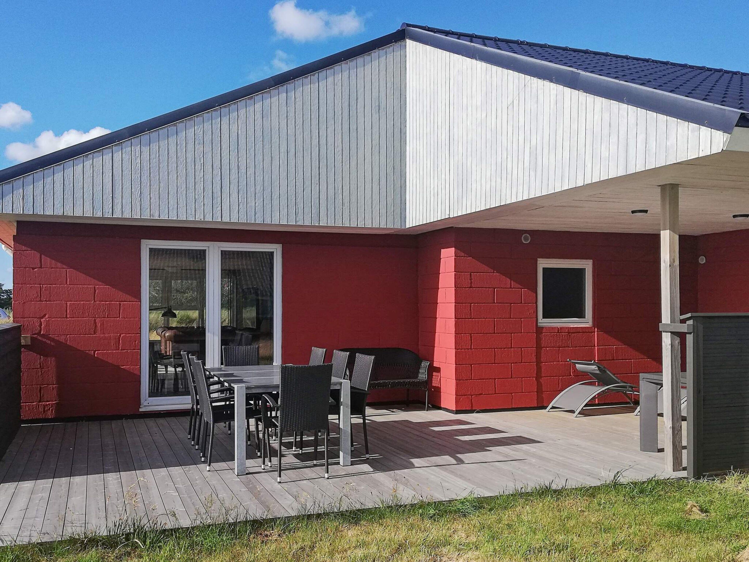 A residential building with a red brick exterior, a covered patio with outdoor furniture, and a sliding glass door leading to an interior space.