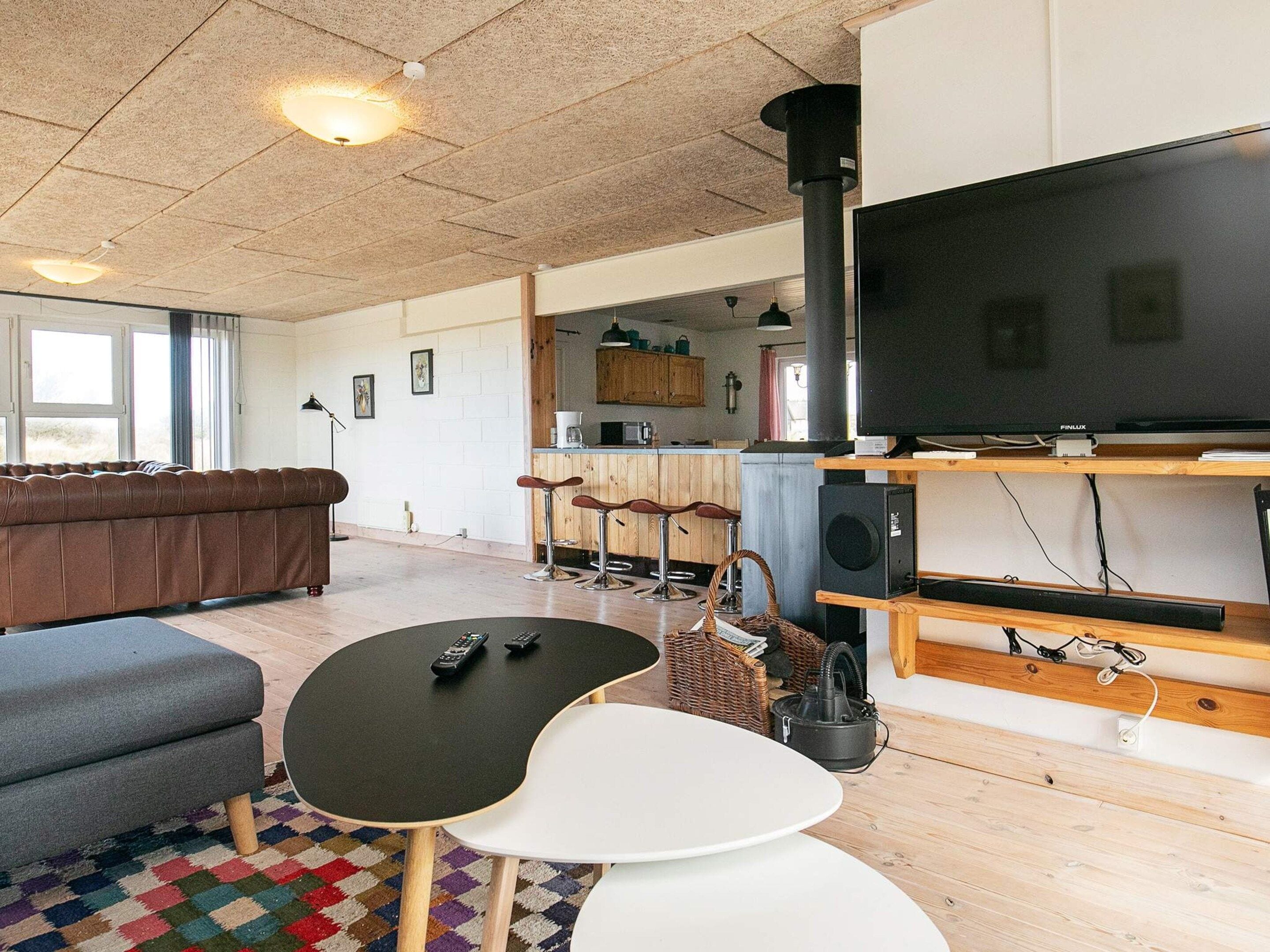 A living room with a sofa, a coffee table, and a TV. There is a kitchen area in the background.