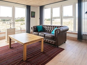 A room with a leather sofa, a wooden coffee table, and a view through large windows.