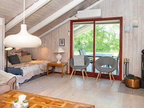 A cozy bedroom with a bed, bedside lamps, a wooden nightstand, and a view through a glass door to an outdoor seating area.