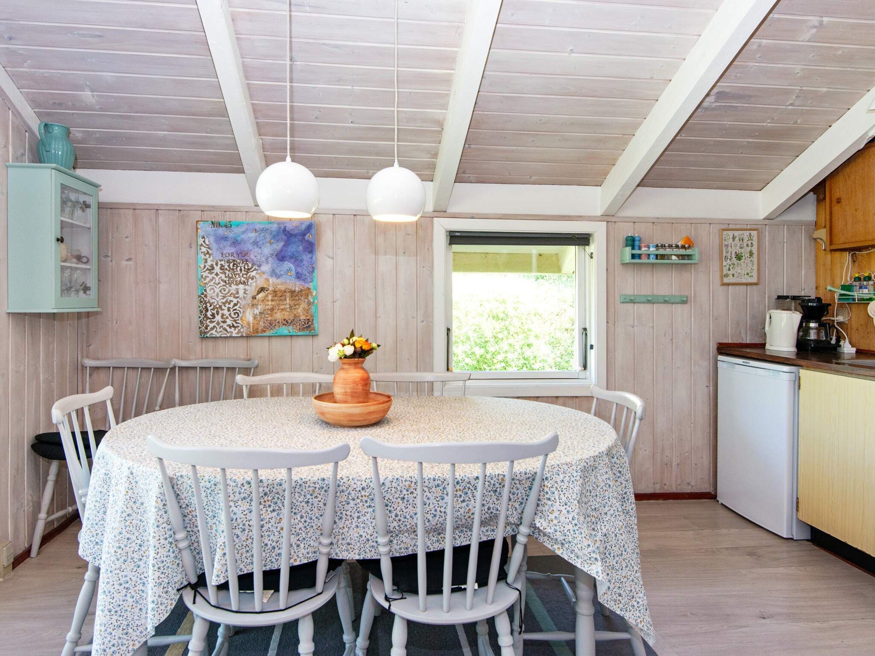 A dining area with a round table, white chairs, a vase with flowers, and a window with a view of greenery.