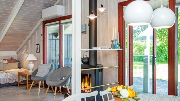 Un salon chaleureux avec une cheminée, une table à manger agrémentée d’un vase de fleurs et un coin salon confortable avec un fauteuil et une lampe.