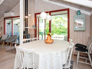 A dining area with a round table, white chairs, a vase with flowers, and a view of greenery outside. - 6 Person Holiday Home in Hemmet (Hemmet)