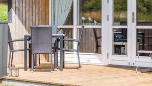 Ein überdachter Außenbereich mit Holzterrasse, einem Tisch mit Stühlen und einer Glastür, die zu einem Innenraum führt.