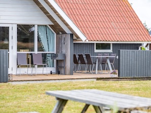 Ein Haus mit überdachter Terrasse, einem Essbereich mit Stühlen und Tisch sowie einem Rasengarten.