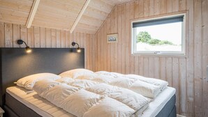 Ein Zimmer mit Holzwänden, einem Bett, zwei Wandleuchten, einem Fenster und einem kleinen Bilderrahmen.