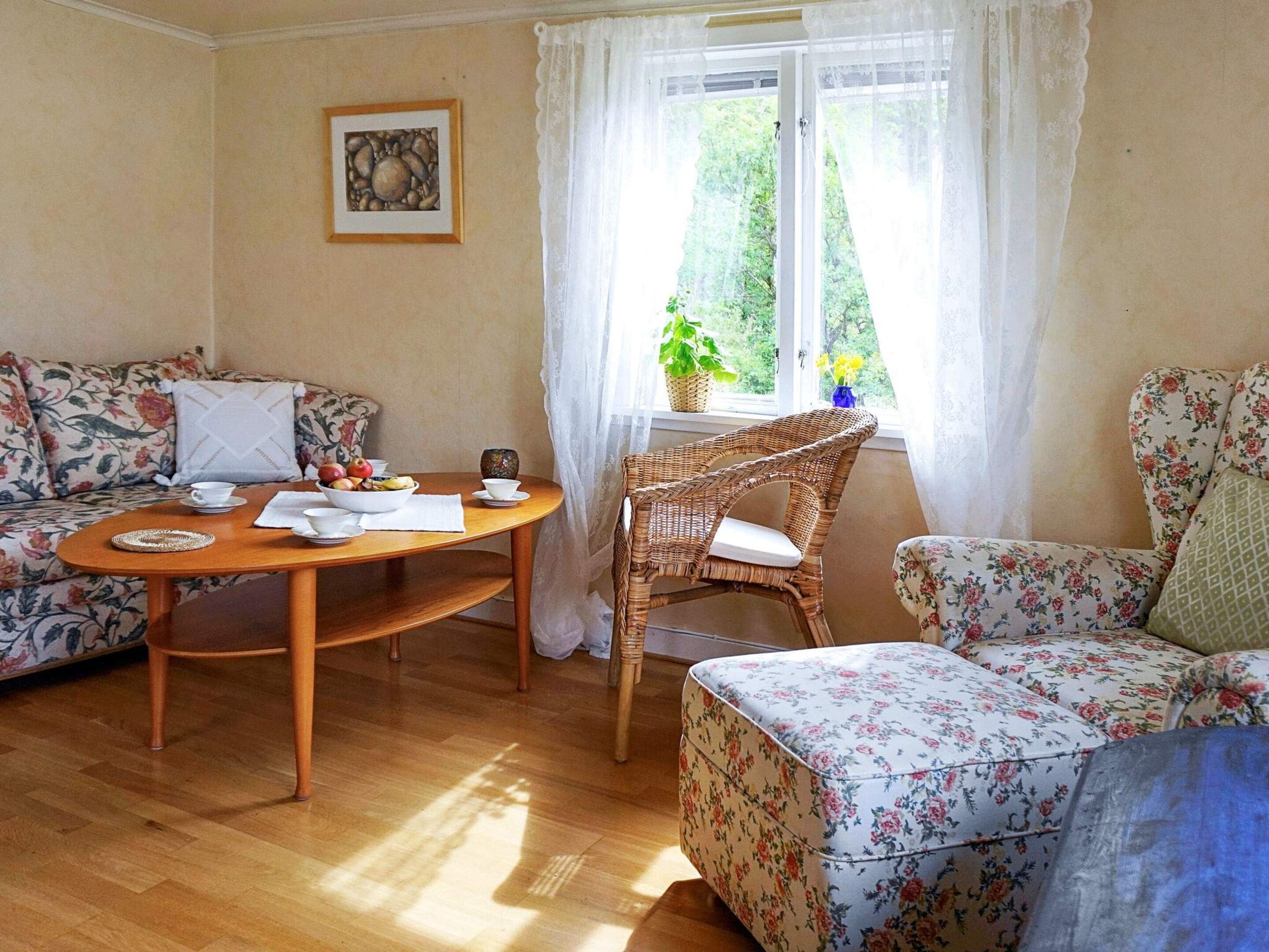 A cozy living room with a sofa, a wicker chair, a round wooden table, and a window with curtains.