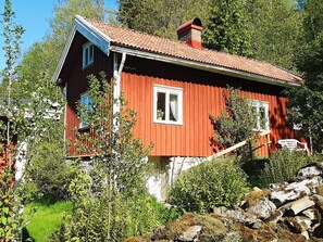 A red wooden house with a sloped roof, surrounded by greenery and rocks. - 6 Person Holiday Home in Henan (Henån)