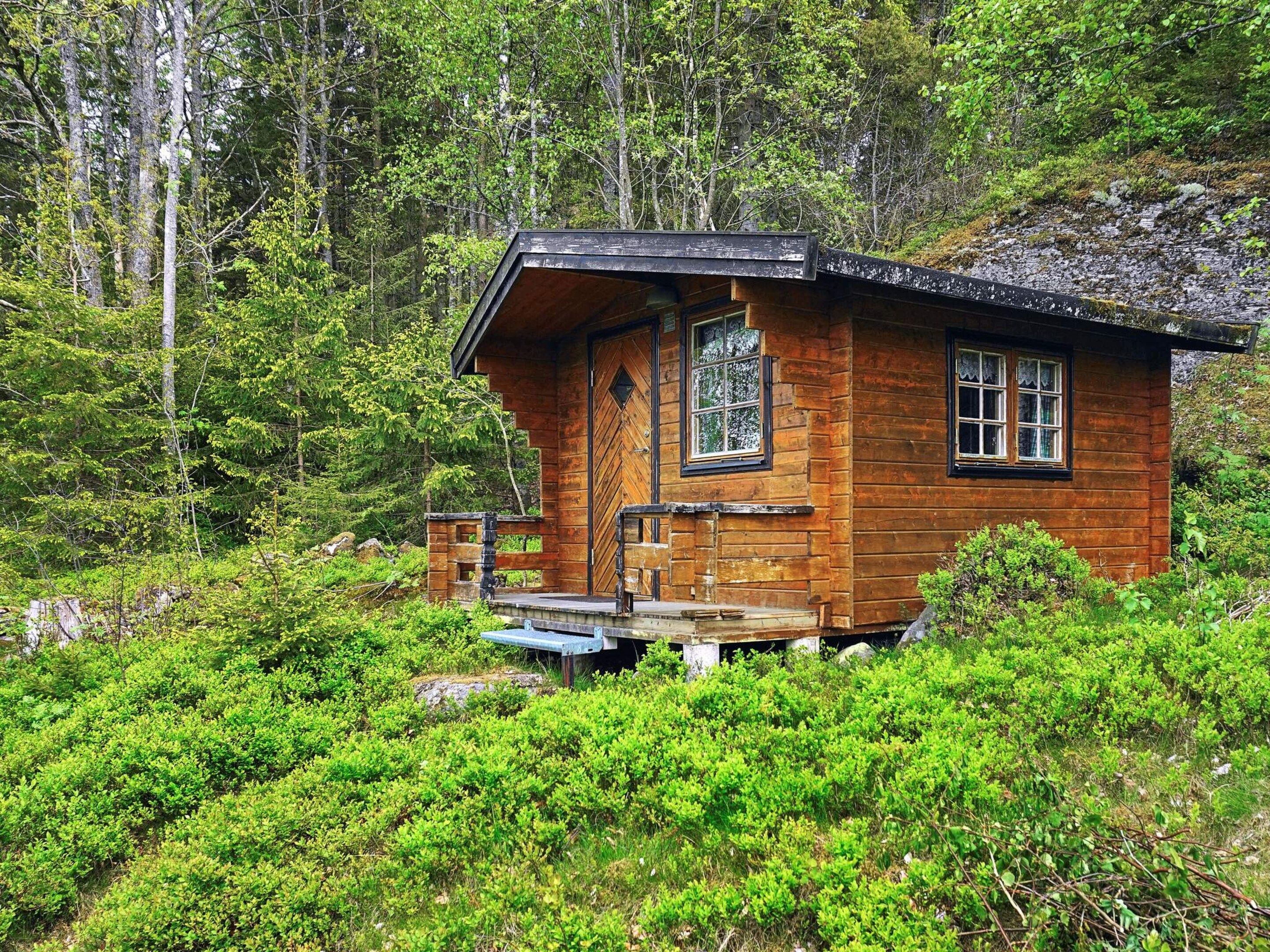 En stuga av trä med en veranda, omgiven av tät skog.