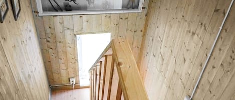 A wooden staircase with a handrail and a view of the upper floor through a window.