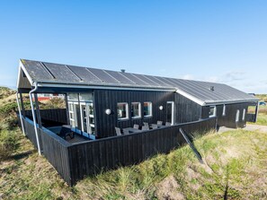 A black wooden building with a sloped roof, large windows, and a covered outdoor seating area. - 8 Person Holiday Home on a Holiday Park in Hvide Sande (Hvide Sande)