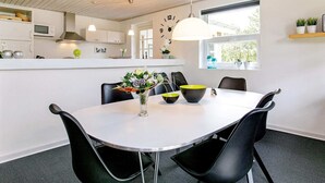 A modern kitchen with white cabinets, a white dining table, black chairs, and a clock on the wall. - Holiday Home in BlÃ¥vand (Blavand)