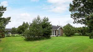 A house with a sloped roof, surrounded by a grassy yard and trees. - Holiday Home in BlÃ¥vand (Blavand)