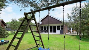 A wooden swing set with two swings and a ladder, set against a house with a covered patio. - Holiday Home in BlÃ¥vand (Blavand)