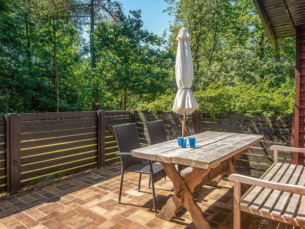 An outdoor patio with a wooden table and chairs, a white umbrella, and a brick floor. - 4 Person Holiday Home in Norre Nebel (Norre Nebel)