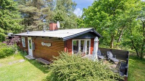 A small cabin with a wooden exterior, a satellite dish, and a patio with outdoor seating. - 4 Person Holiday Home in Norre Nebel (Norre Nebel)