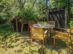 An outdoor seating area with a round table and four chairs, surrounded by lush greenery and a wooden fence.
