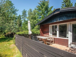 Une cabane en bois dotée d’une terrasse, de mobilier d’extérieur et d’une grande fenêtre.
