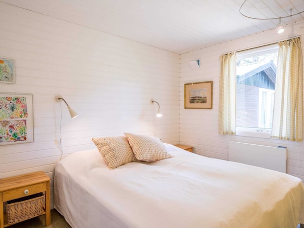 Et soveværelse med seng, to sengeborde med lamper, et bord med en kurv og et vindue med gardiner.