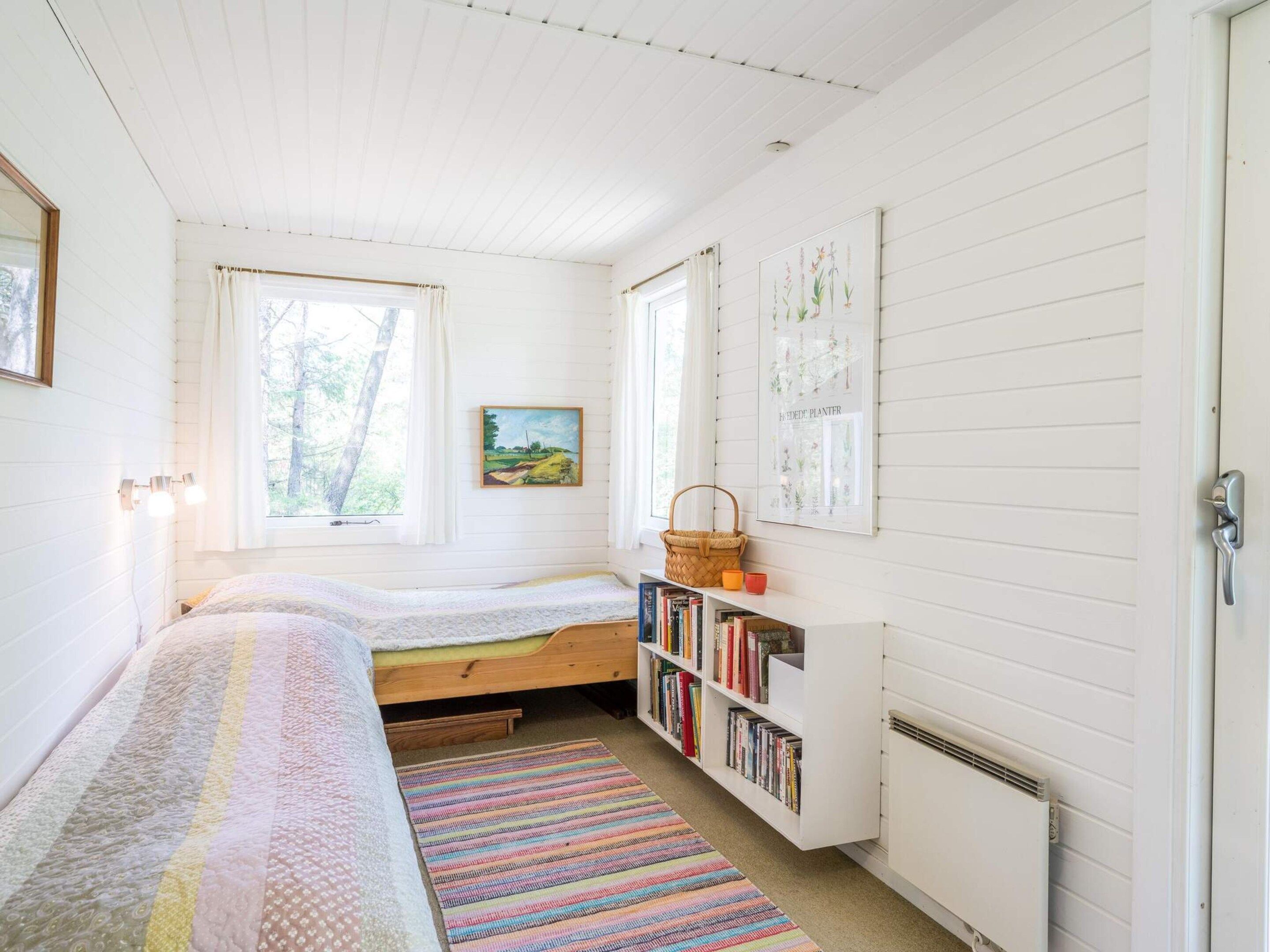 Un dormitorio con dos camas, una estantería y una ventana con cortinas.