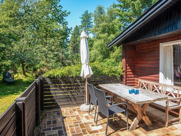 A wooden deck with a table and chairs, surrounded by a wooden fence and lush greenery. - 4 Person Holiday Home in Norre Nebel (Norre Nebel)