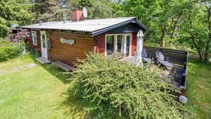 A small cabin with a wooden exterior, a satellite dish, and a deck with outdoor seating. - 4 Person Holiday Home in Norre Nebel (Norre Nebel)