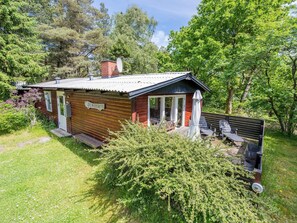 A small cabin with a wooden exterior, a satellite dish, and a deck with outdoor seating. - 4 Person Holiday Home in Norre Nebel (Norre Nebel)