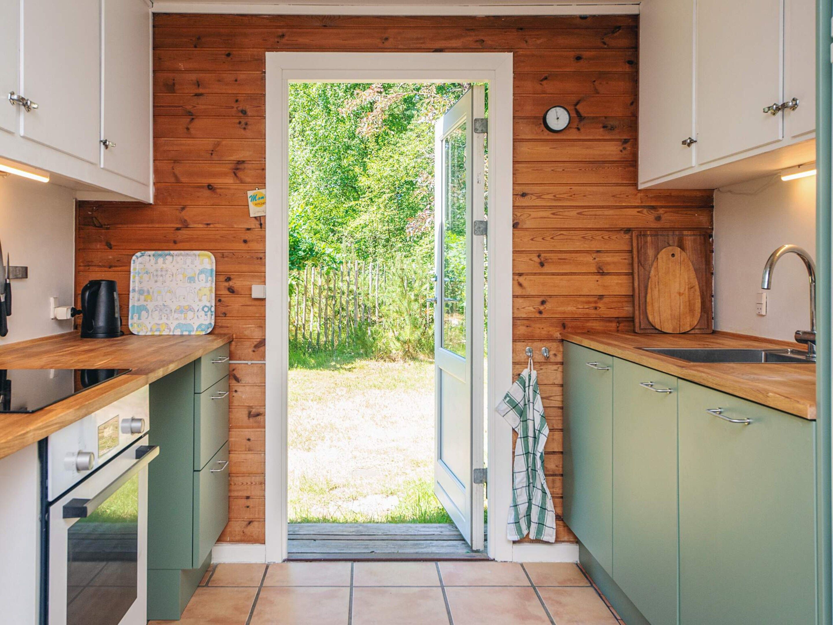 A kitchen with wooden walls, a large window, and a view of greenery outside.