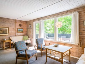 A cozy room with a wooden interior, a sofa, two chairs, a table, and a large window with a view of greenery. - 4 Person Holiday Home in Norre Nebel (Norre Nebel)