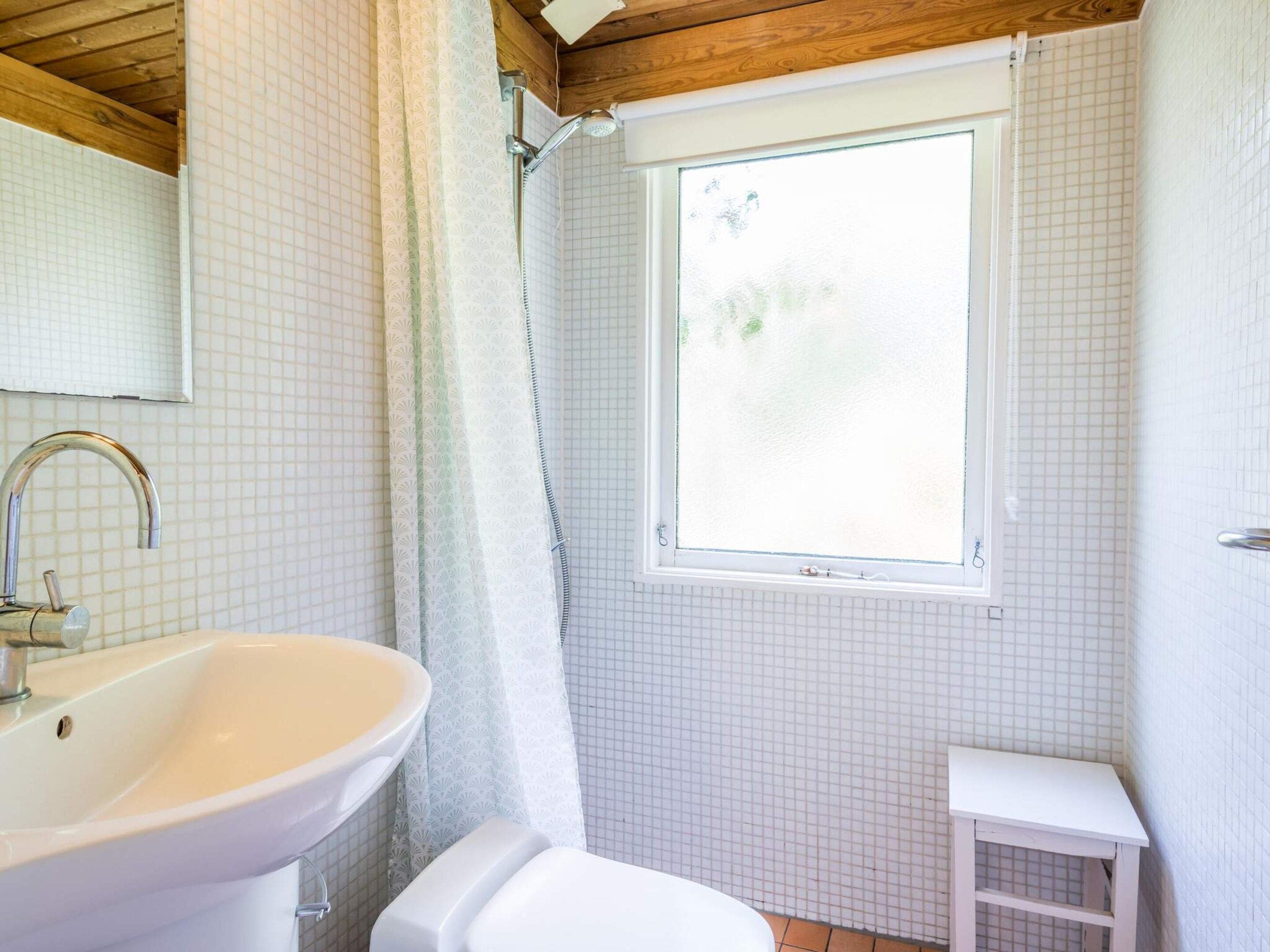 Ein Badezimmer mit weißem Waschbecken, Toilette, einer Dusche mit Glastür und einem Fenster für natürliches Licht.