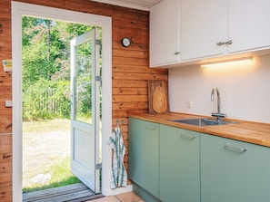 Una cocina con paredes de madera, una puerta blanca que da al exterior, una encimera verde y un reloj colgado en la pared.