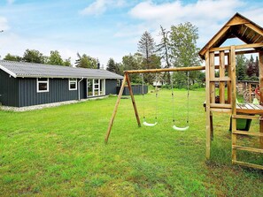 Een woonhuis met een houten schommel, een speeltuintje en een woning met een metalen dak.