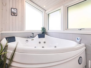 Een moderne badkamer met een groot, wit bad, een kleine potplant en een raam met geëtste glas.