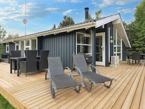 Een modern terras buiten met een eettafel, stoelen, een barbecue en een overdekt zitgedeelte.