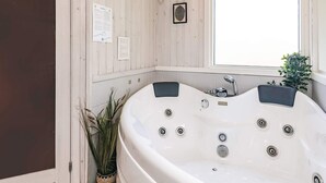 A large white bathtub with multiple jets, a window above it, and a small plant beside it. - Holiday Home in VÃ¦ggerlÃ¸se (Vaeggerlose)
