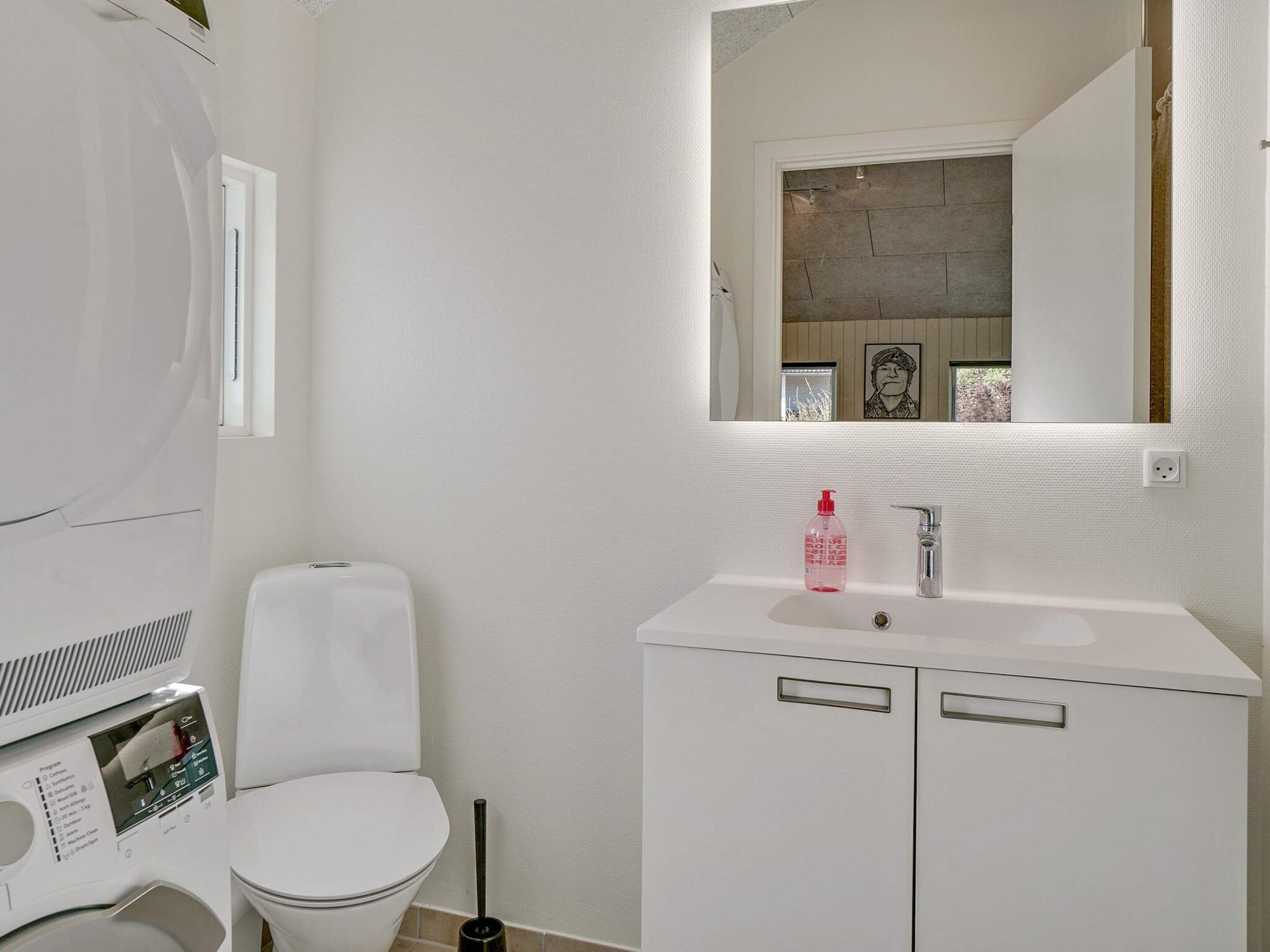 A bathroom with a toilet, a sink with a mirror above it, and a wall-mounted heater.