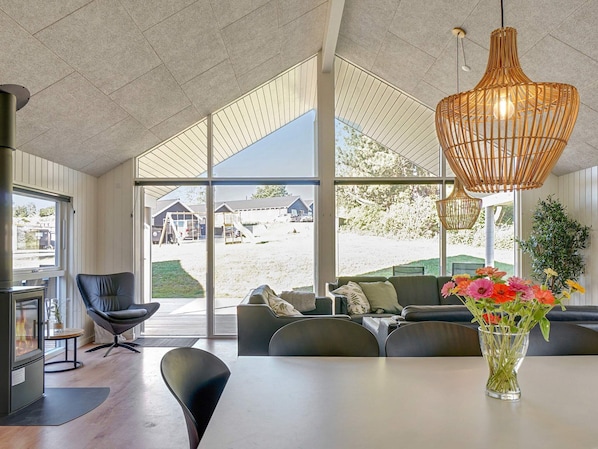 A modern interior with a dining area, sofas, and a large window offering a view of a playground.