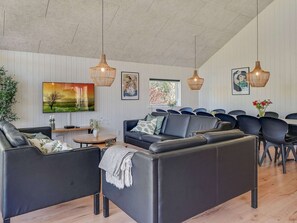 A modern living room with a sofa, chairs, a TV, artwork, and pendant lights.