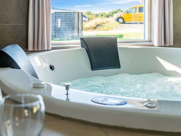 A hot tub with a control panel, a glass of water, and a view of a yellow car outside.