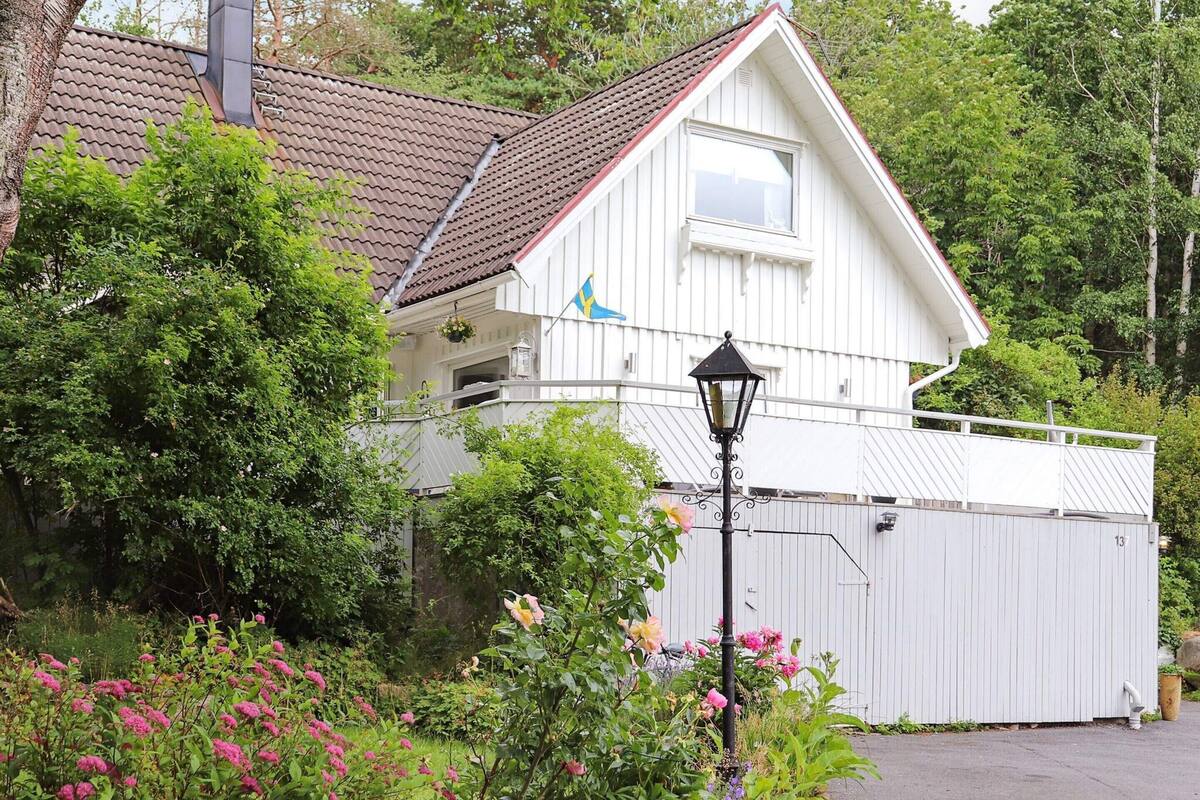 A white house with a red roof, a balcony, and a garden with pink flowers.
