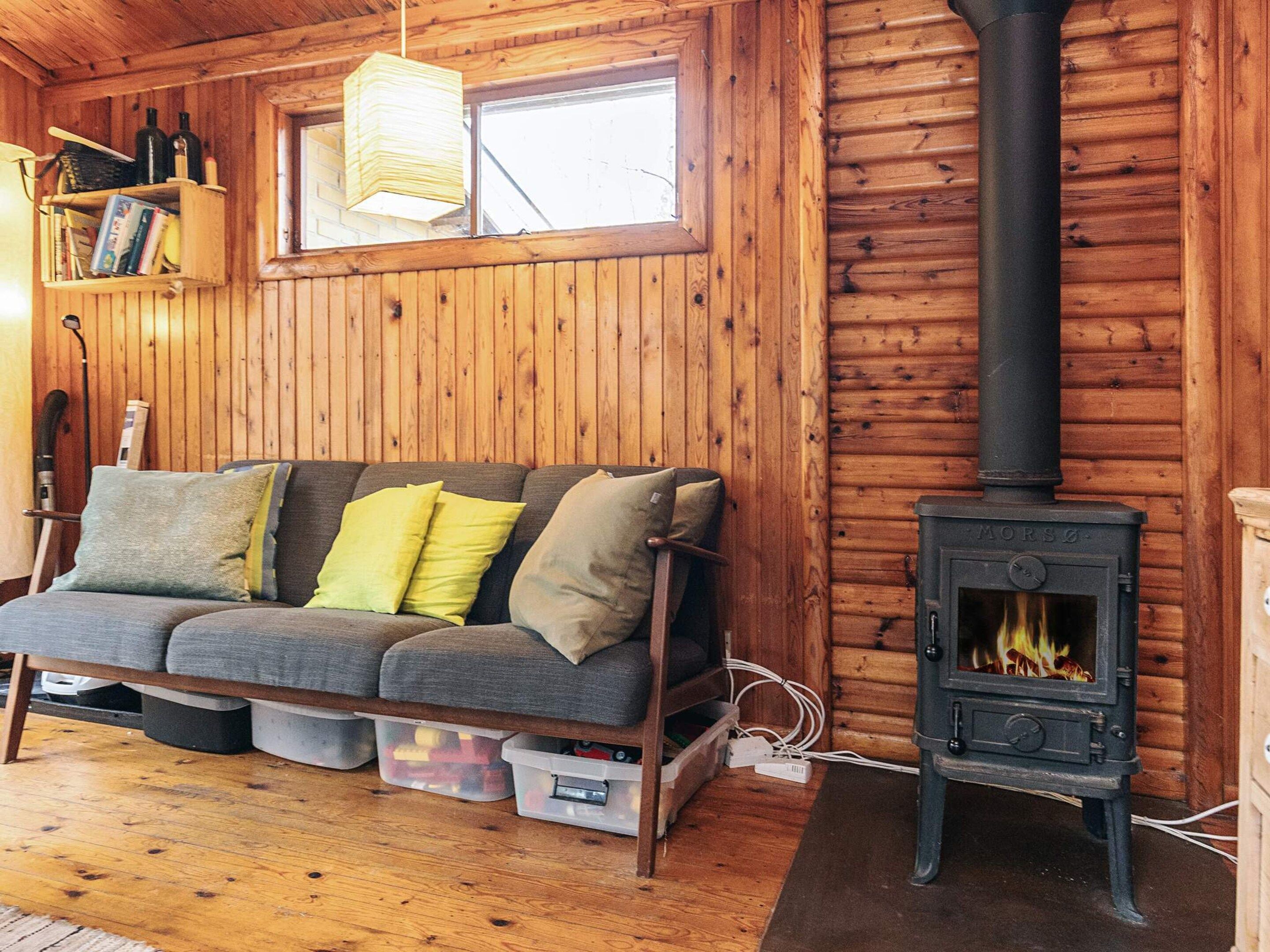 Interior de una cabaña de madera con sofá, chimenea y ventana.