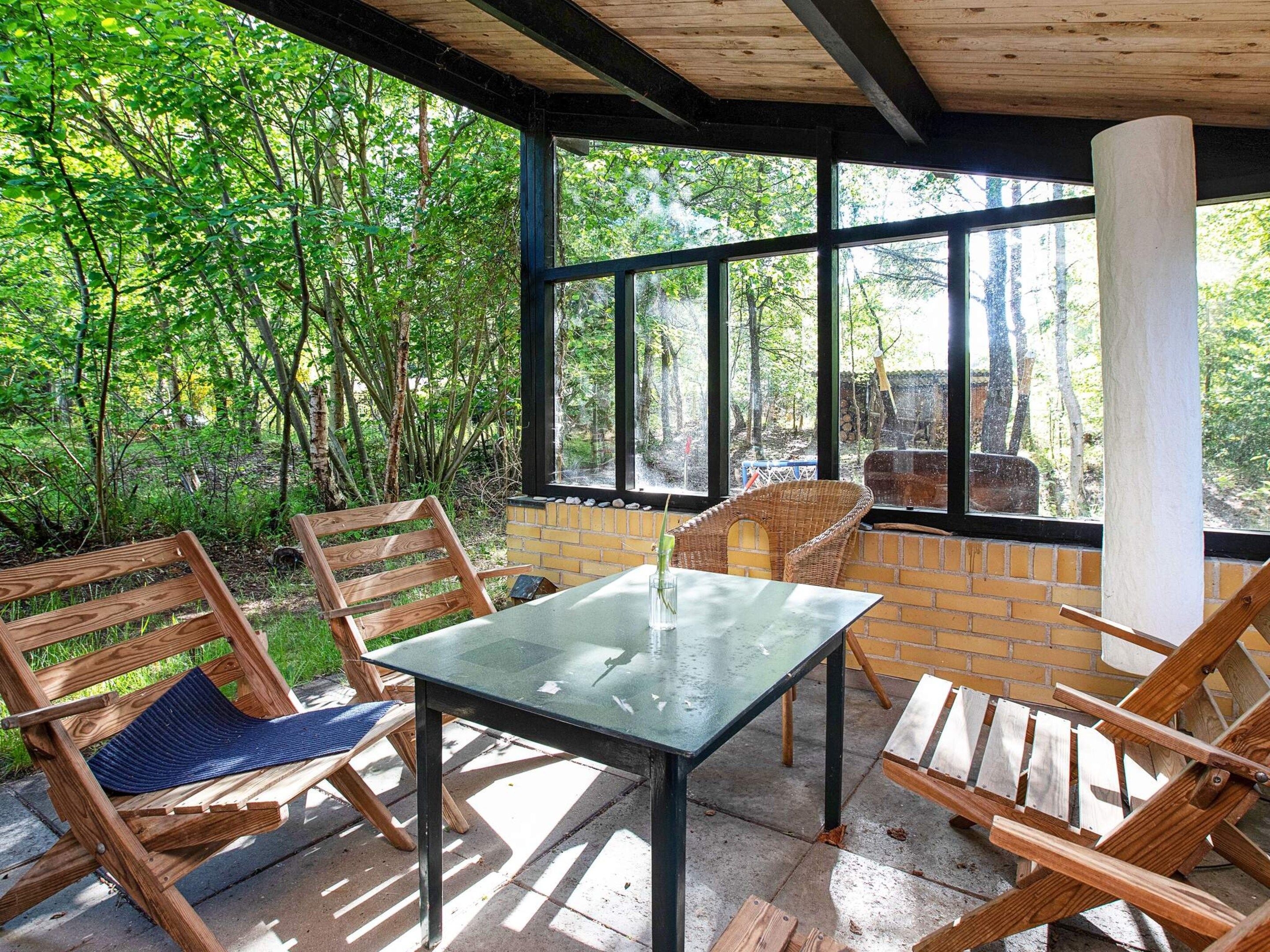Un área de estar al aire libre con una mesa y sillas, rodeada por un muro de ladrillo y ventanas grandes.