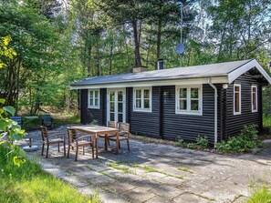 A cabin with a patio, wooden furniture, and a natural forest backdrop. - 8 Person Holiday Home in Vaeggerlose (Vaeggerlose)