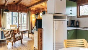 A wooden cabin interior with a dining area, a kitchen with a refrigerator, and a window. - 8 Person Holiday Home in Vaeggerlose (Vaeggerlose)