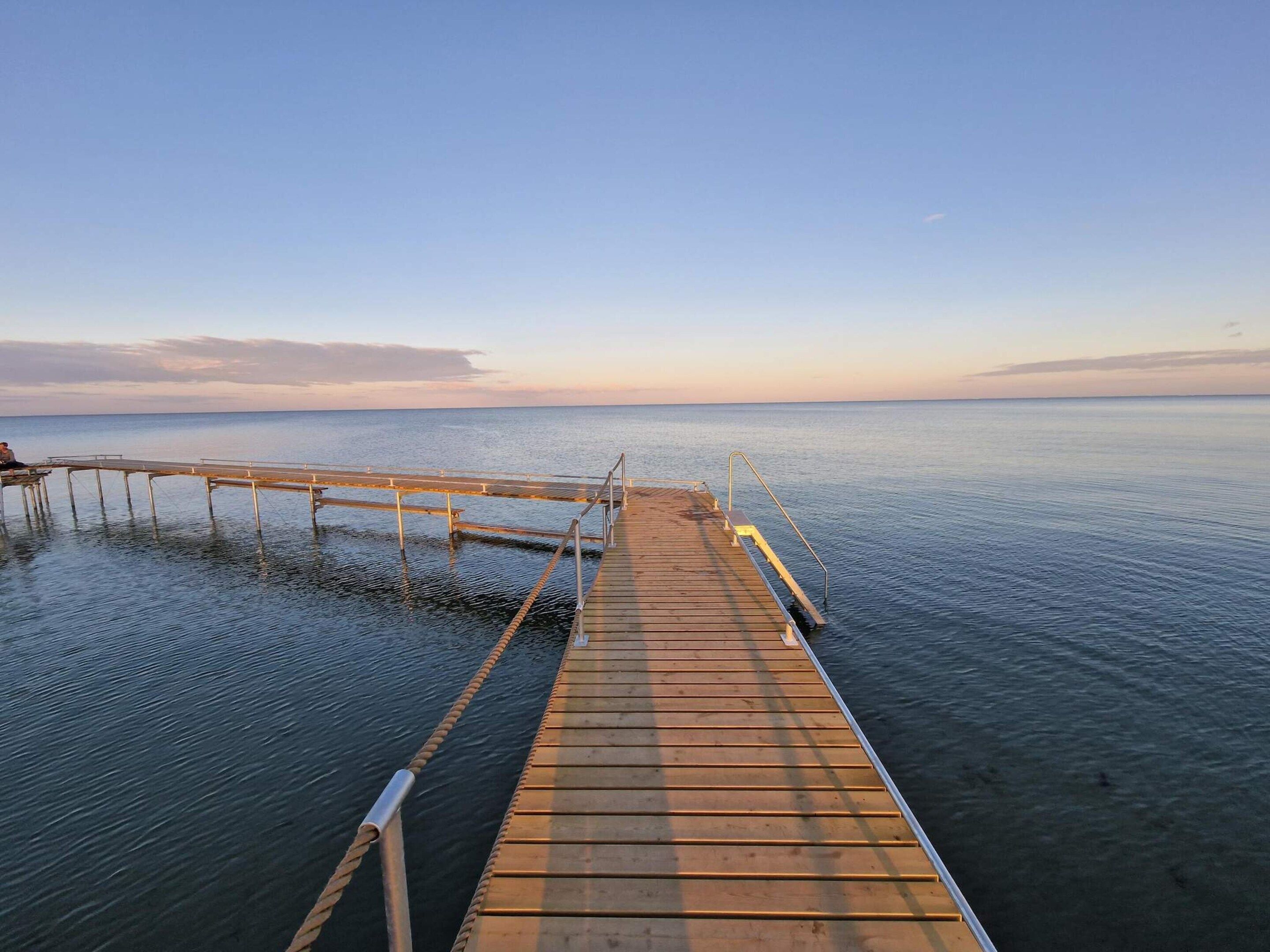 A wooden pier extending into calm water with a clear sky above.