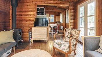 Een vakantiehuisje van binnen met een open haard, een televisie, een eethoek en een groot raam.