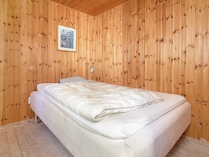 A room with wooden panel walls, a bed with white bedding, a single bedside lamp, and a framed picture on the wall.