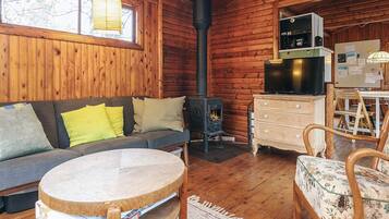 A cozy cabin interior with a sofa, a round wooden table, a fireplace, and a kitchenette.