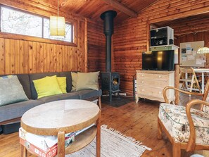 A cozy cabin interior with a sofa, a round wooden table, a fireplace, and a kitchenette. - 8 Person Holiday Home in Vaeggerlose (Vaeggerlose)