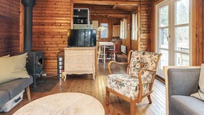 A log cabin interior with a fireplace, a television, a dining area, and a large window. - 8 Person Holiday Home in Vaeggerlose (Vaeggerlose)